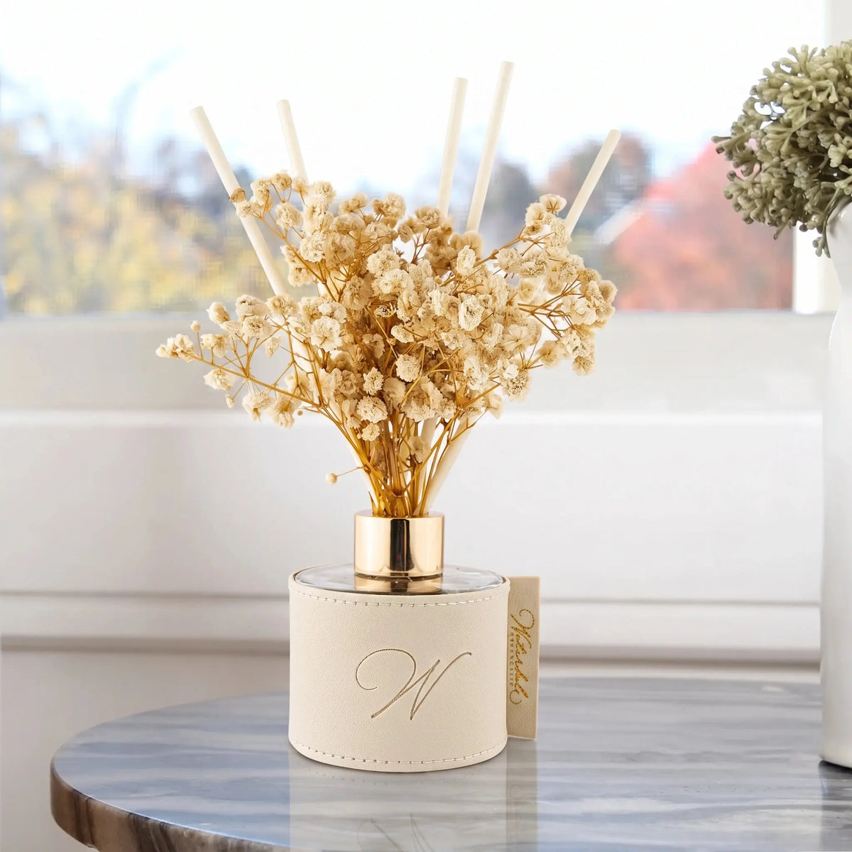 Taupe leatherette reed diffuser with dried flowers on a marble side table by a sunny window