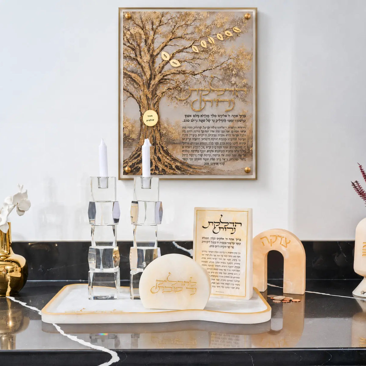 Hadlokas Neiros family tree hung above a Shabbos candle setup with crystal candlesticks, a marble tray and a tzedakah box