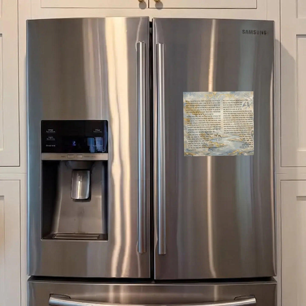 Painted Nishmas magnet from Waterdale Collection, faux leather with deer at a stream, birds and gold leaf behind the Hebrew text on a silver refrigerator in the kitchen.
