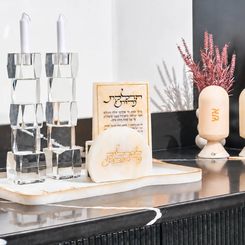 Gold resin Shabbat candle lighting set on a black counter with crystal candlesticks, a Hadlakas Neiros block, and match and spice cloches