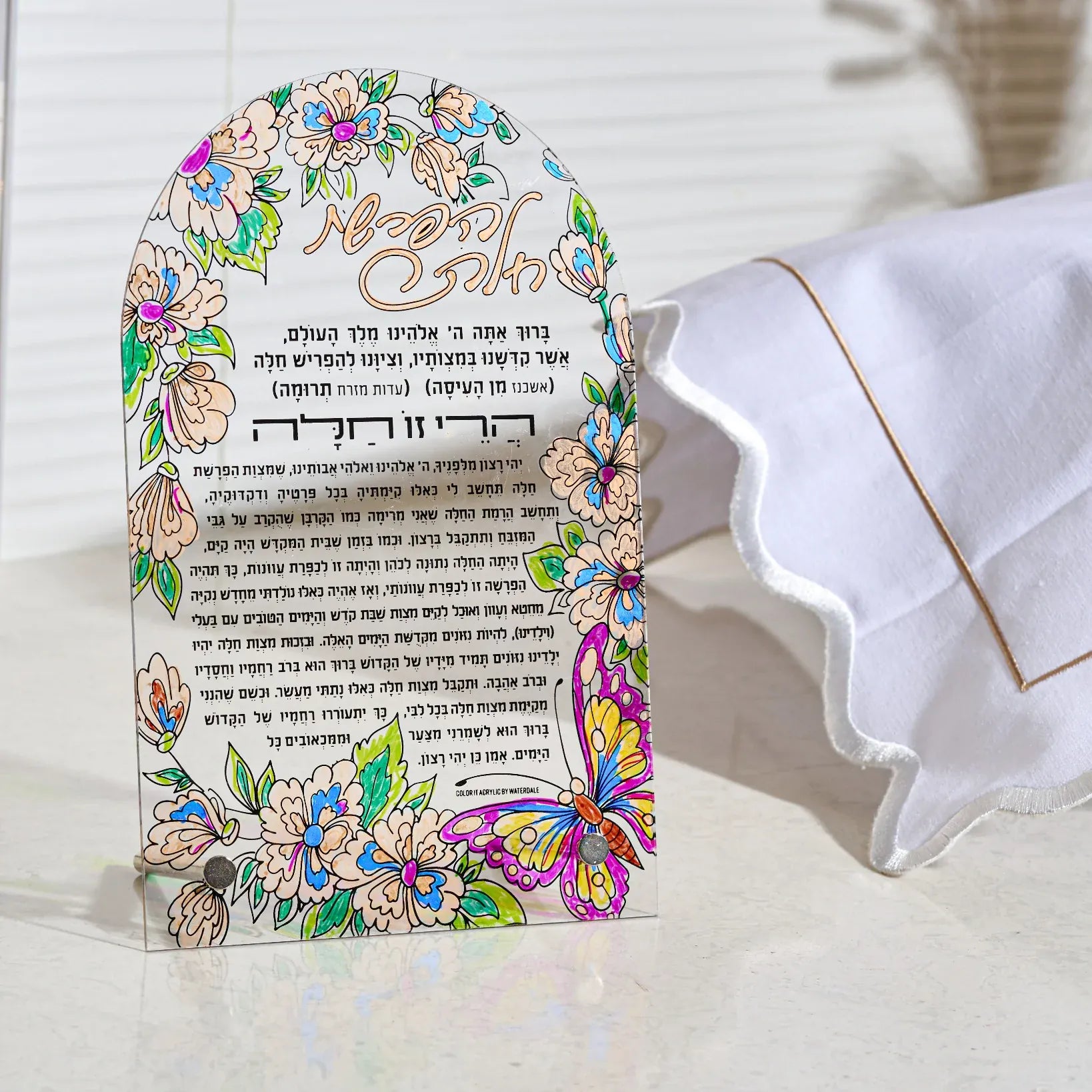 A decorative hafroshas challah lucite craft card for bas mitzvah with colorful floral and butterfly illustrations, featuring Hebrew and English text, displayed next to a challah bake