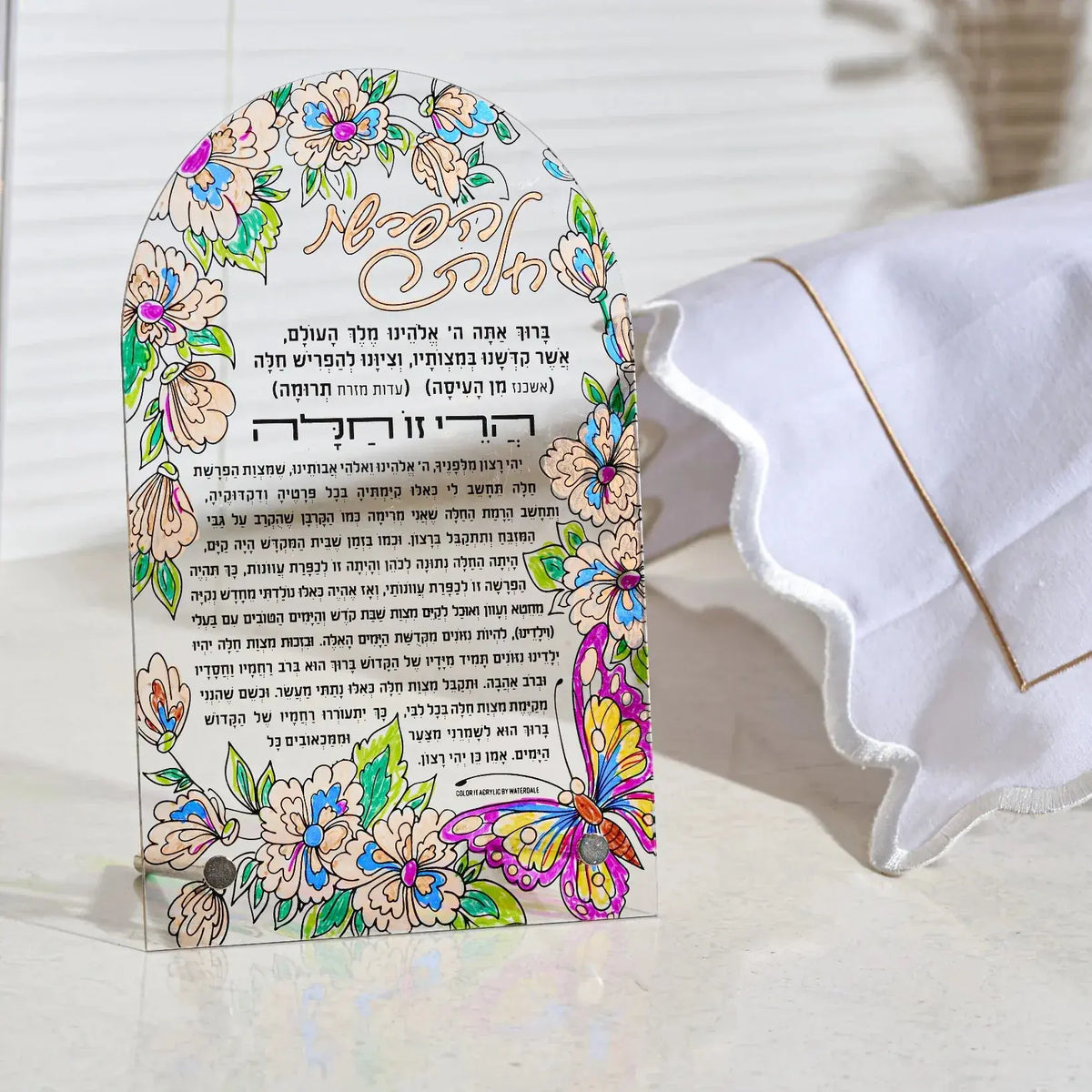 A decorative hafroshas challah lucite craft card for bas mitzvah with colorful floral and butterfly illustrations, featuring Hebrew and English text, displayed next to a challah bake