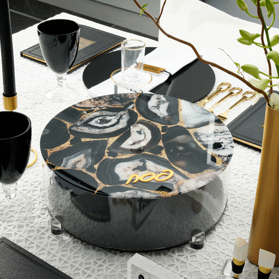 Black agate matzah box with gold veining and lucite lid, displayed on white surface with tabletop styling for Pesach.