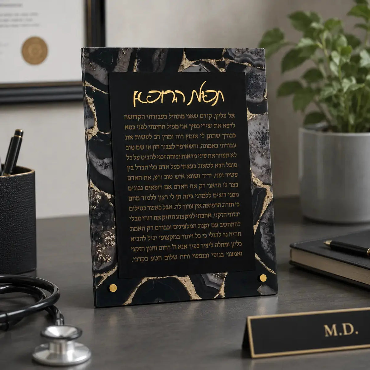 Black agate tabletop plaque with gold veining featuring Hebrew Birchas Harofeh prayer text, displayed on office desk with stethoscope and medical nameplate.