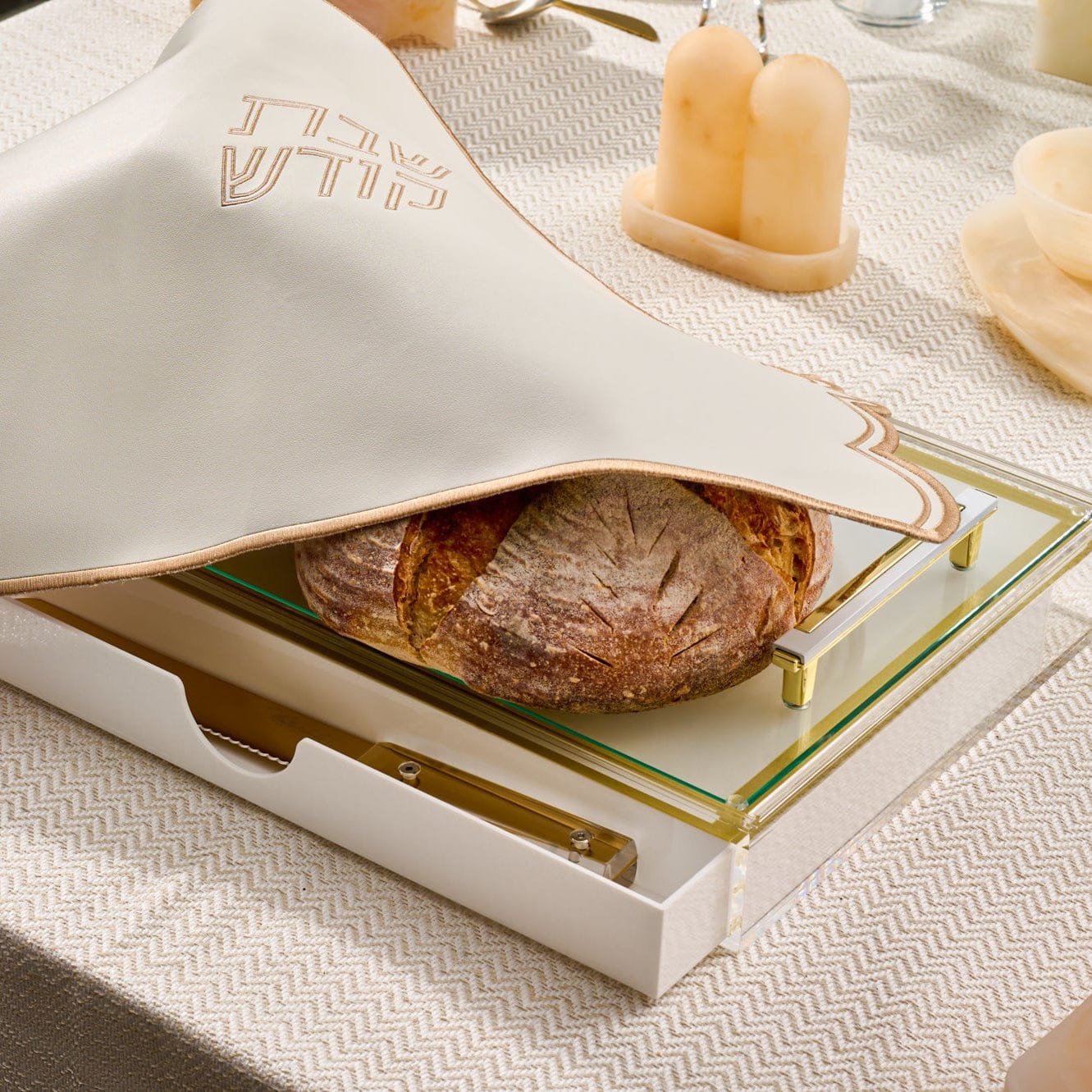 Classic challah board with built-in drawer, featuring a frosted “Shabbat Kodesh” challah cover, elevated glass cutting surface with gold-tone hardware, and artisan challah bread on display.