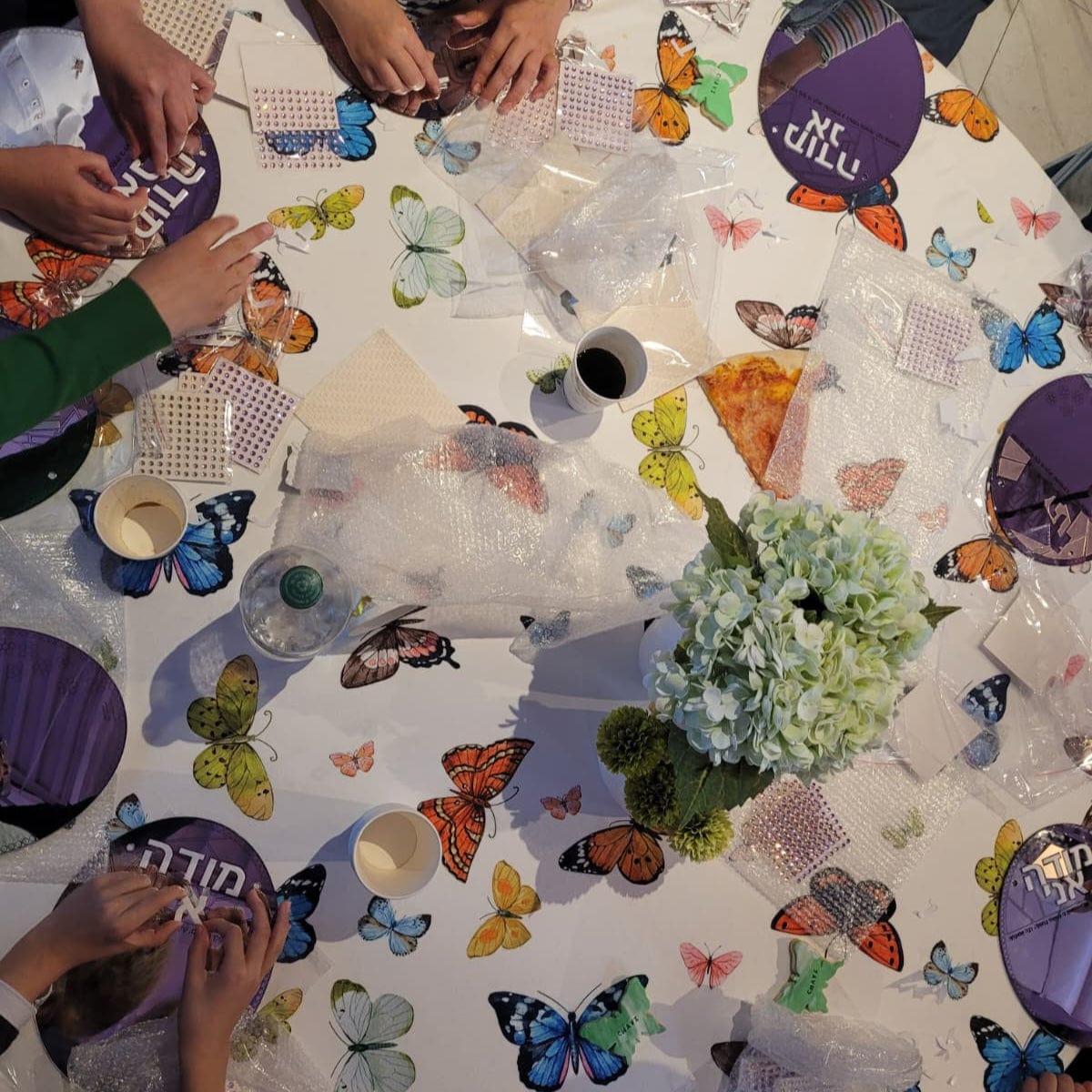 Children crafting at a butterfly-themed table doing Color it Acrylic Mosaic Modeh Ani.