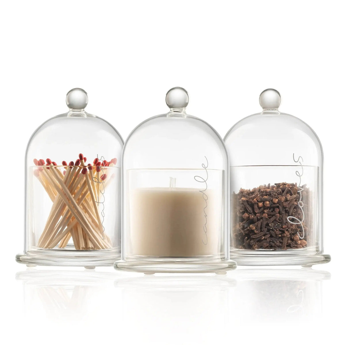 Three glass cloches with knob finials containing red-tipped matches, a white candle, and cloves for a Havdalah ceremony set.