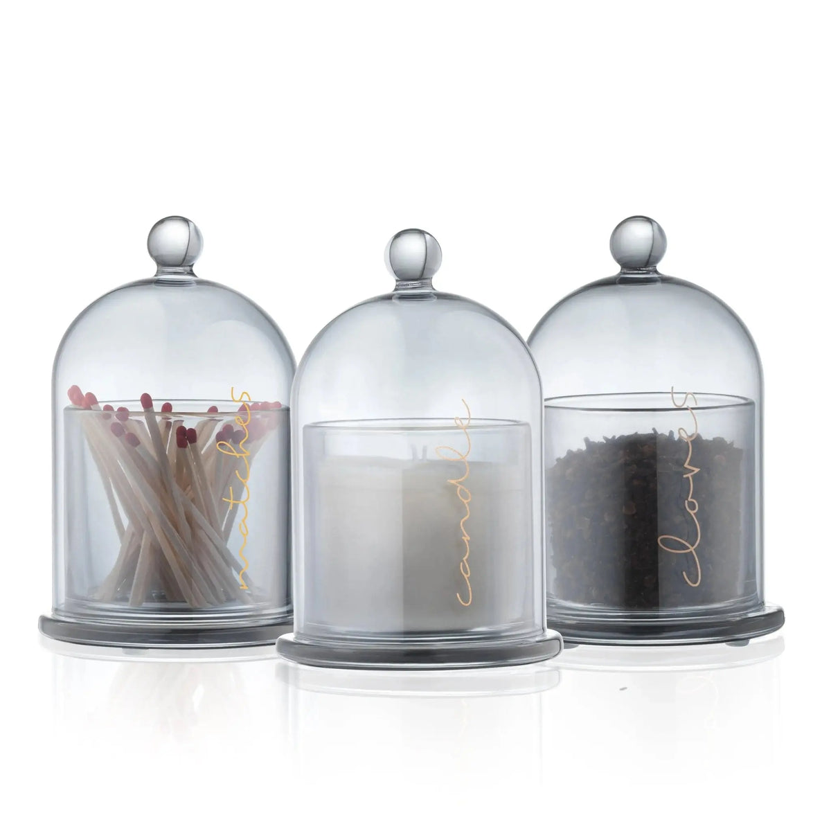 Three glass cloches containing havdalah set items: dried herbs, white candles, and dark spices for Shabbat ritual.