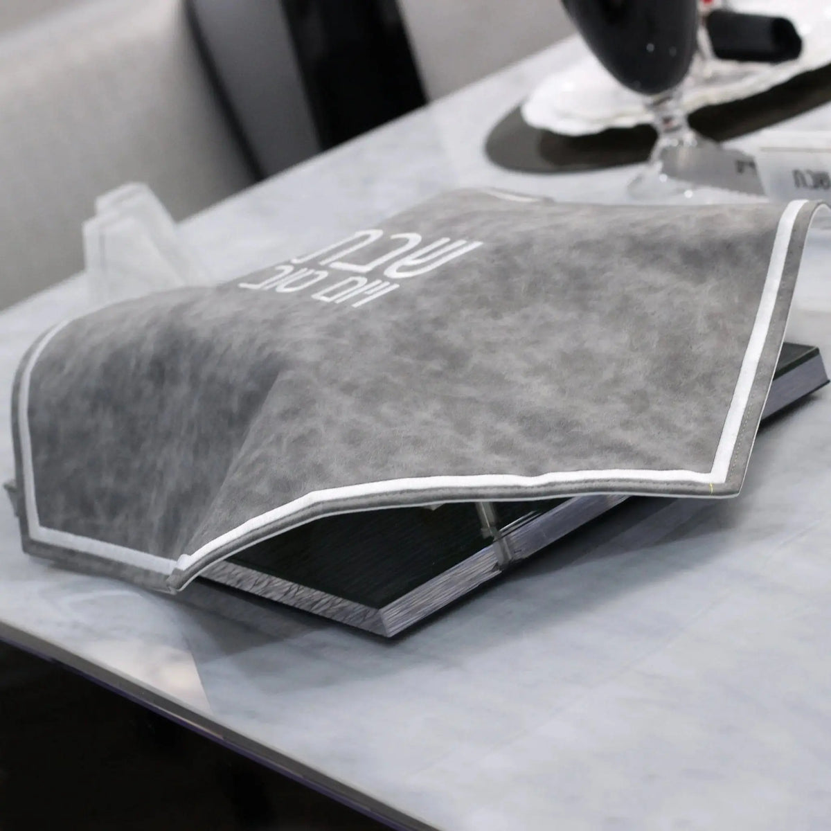 Marbleized gray and white Hexagon Challah Cover with leather trim displayed on a table, ready for Shabbat use.