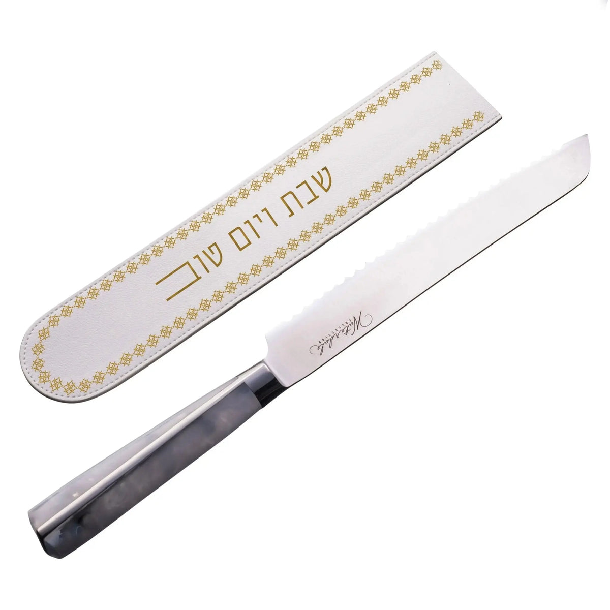 White leather knife blade cover with gold geometric border design and Hebrew text, displayed with dark handle knife.