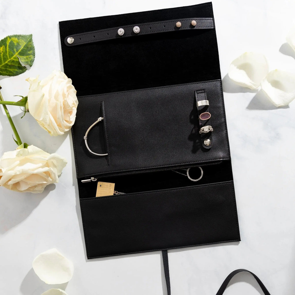 Black leather jewelry roll organizer with multiple compartments displaying rings, necklaces, and bracelets from Waterdale Collection.