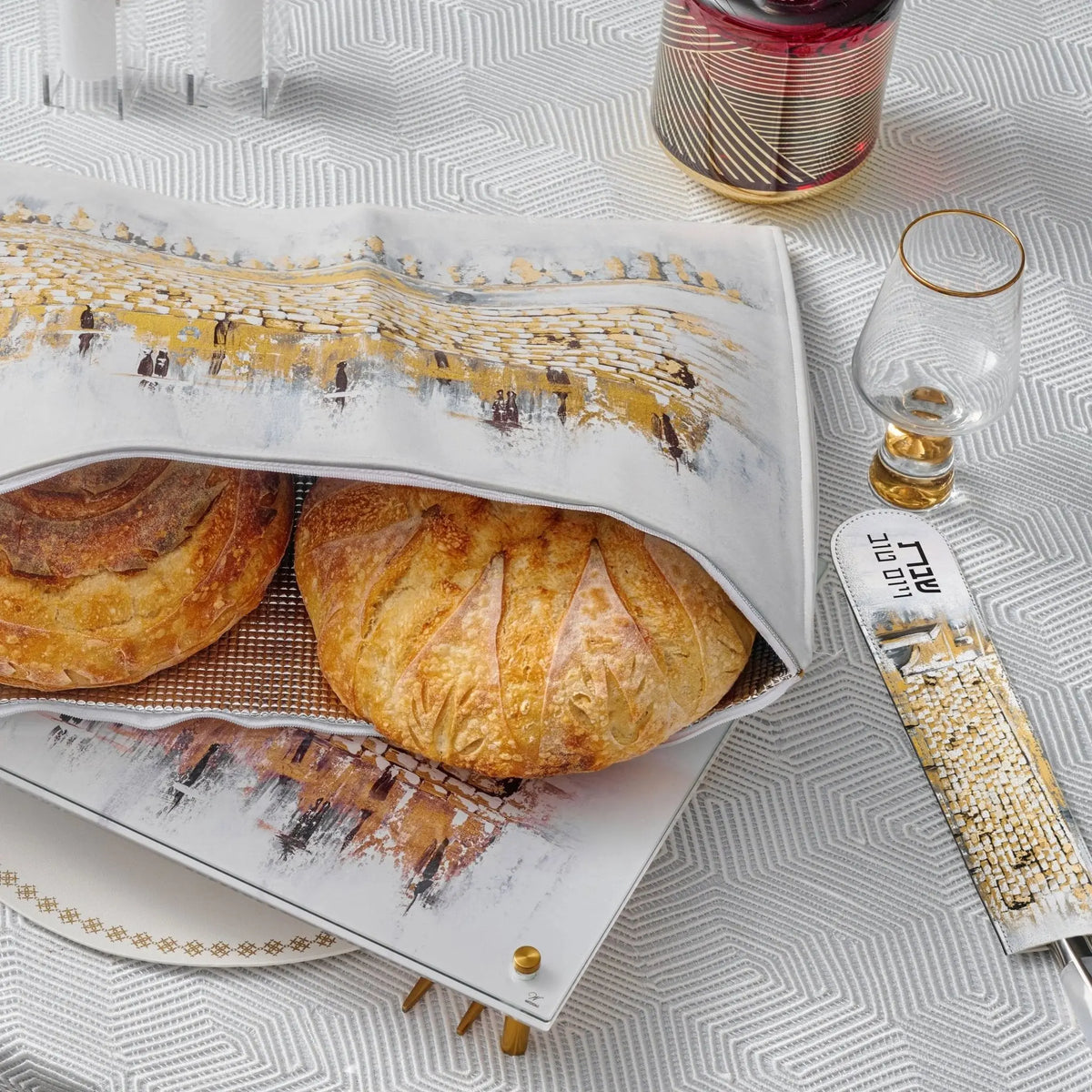 Kosel at Winter painted challah set featuring two golden braided loaves on white ceramic platter with artistic landscape design, displayed with gold accessories.