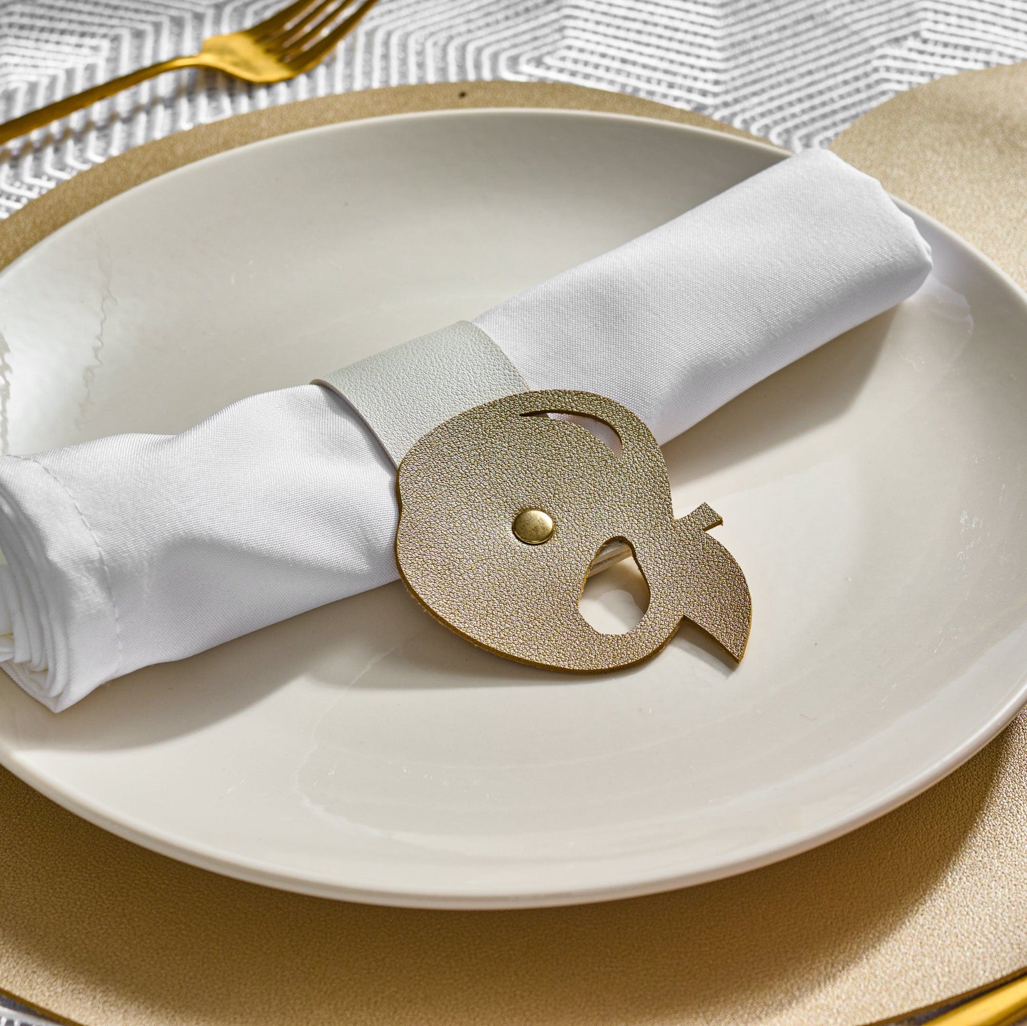 Gold Leather Simanim Napkin Wrap on top of a white plate and Gold leather charger