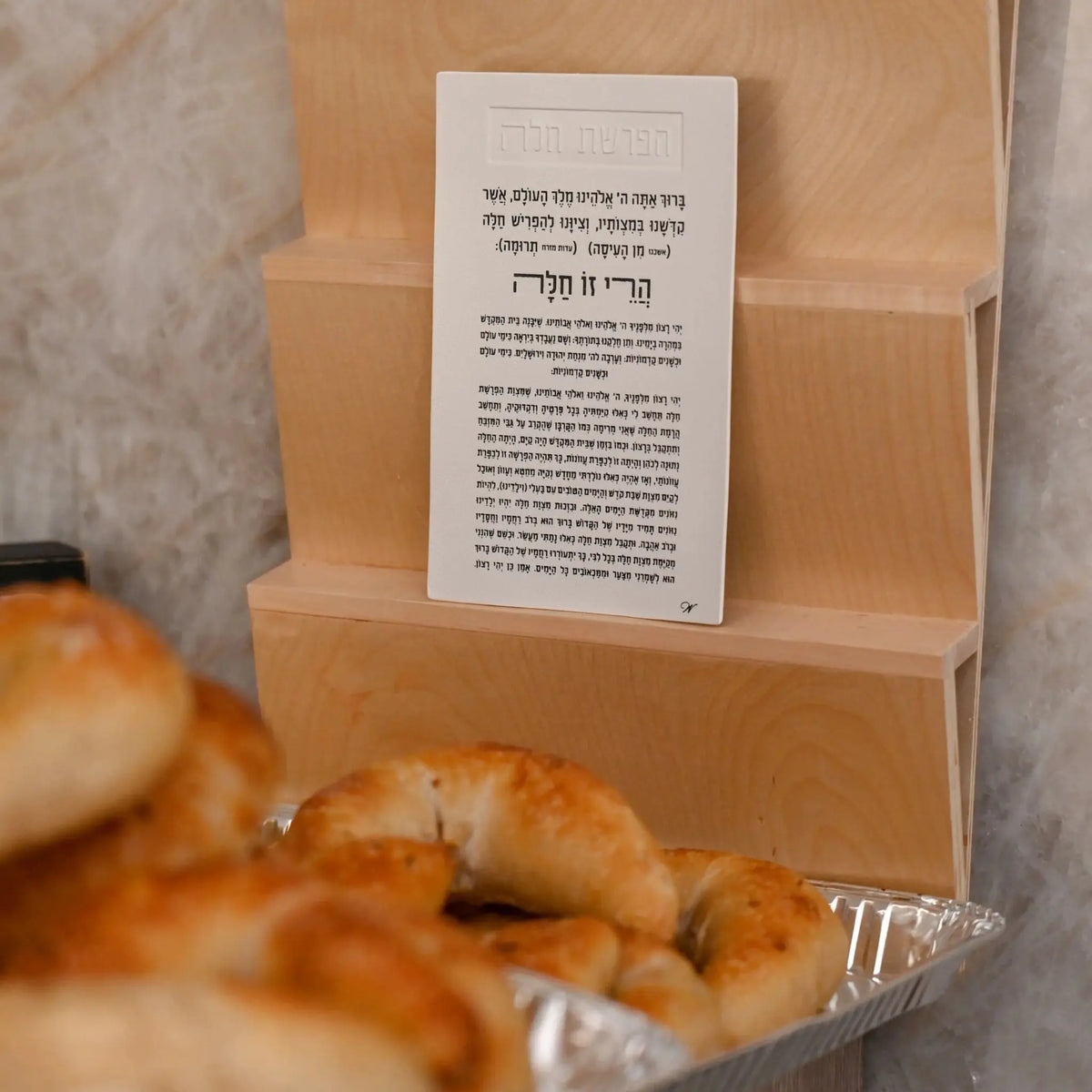 Tan leather Hafrashas Challah magnet with printed blessing text displayed in retail packaging with challah rolls visible below.