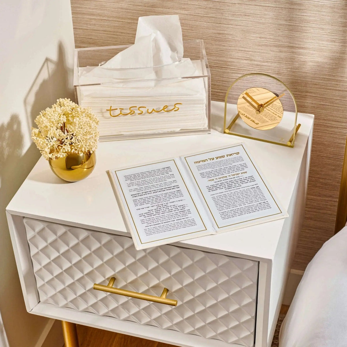 Leather Kriyas Shema prayer book in tan displayed on white nightstand with prayer cards and gold home decor accessories.