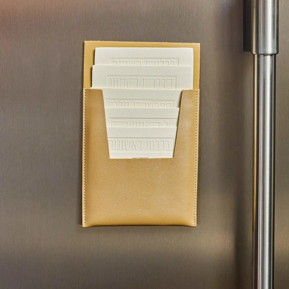 Tan leather magnetic brachos set displayed on refrigerator showing white printed cards for Jewish blessings by Waterdale Collection