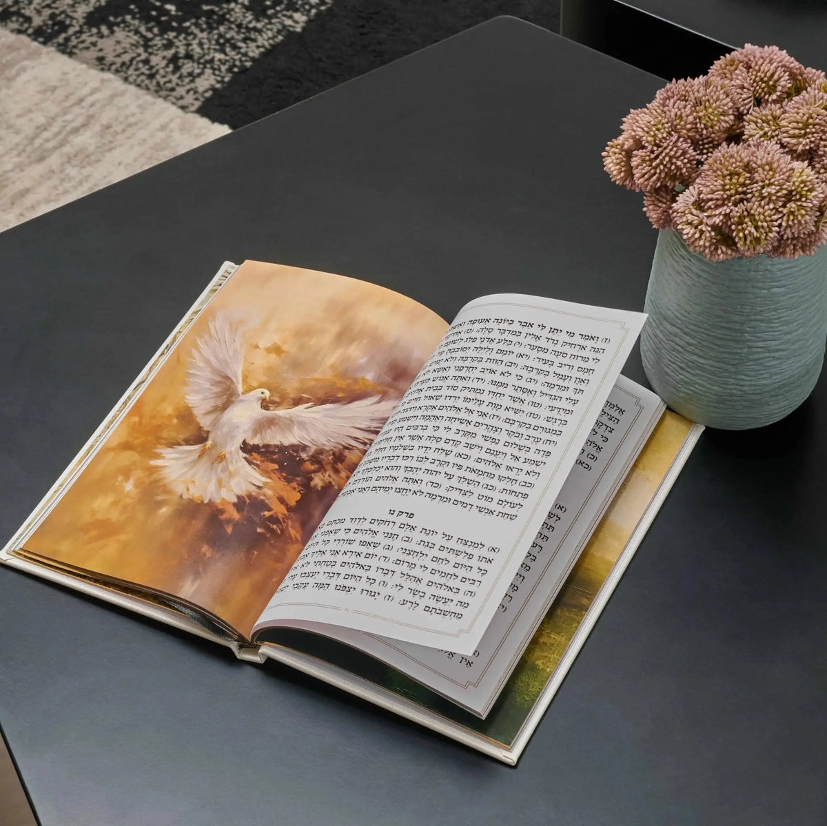 Leather Painted Tehillim book open showing illustrated Hebrew text pages, displayed on dark surface with decorative candle holder nearby
