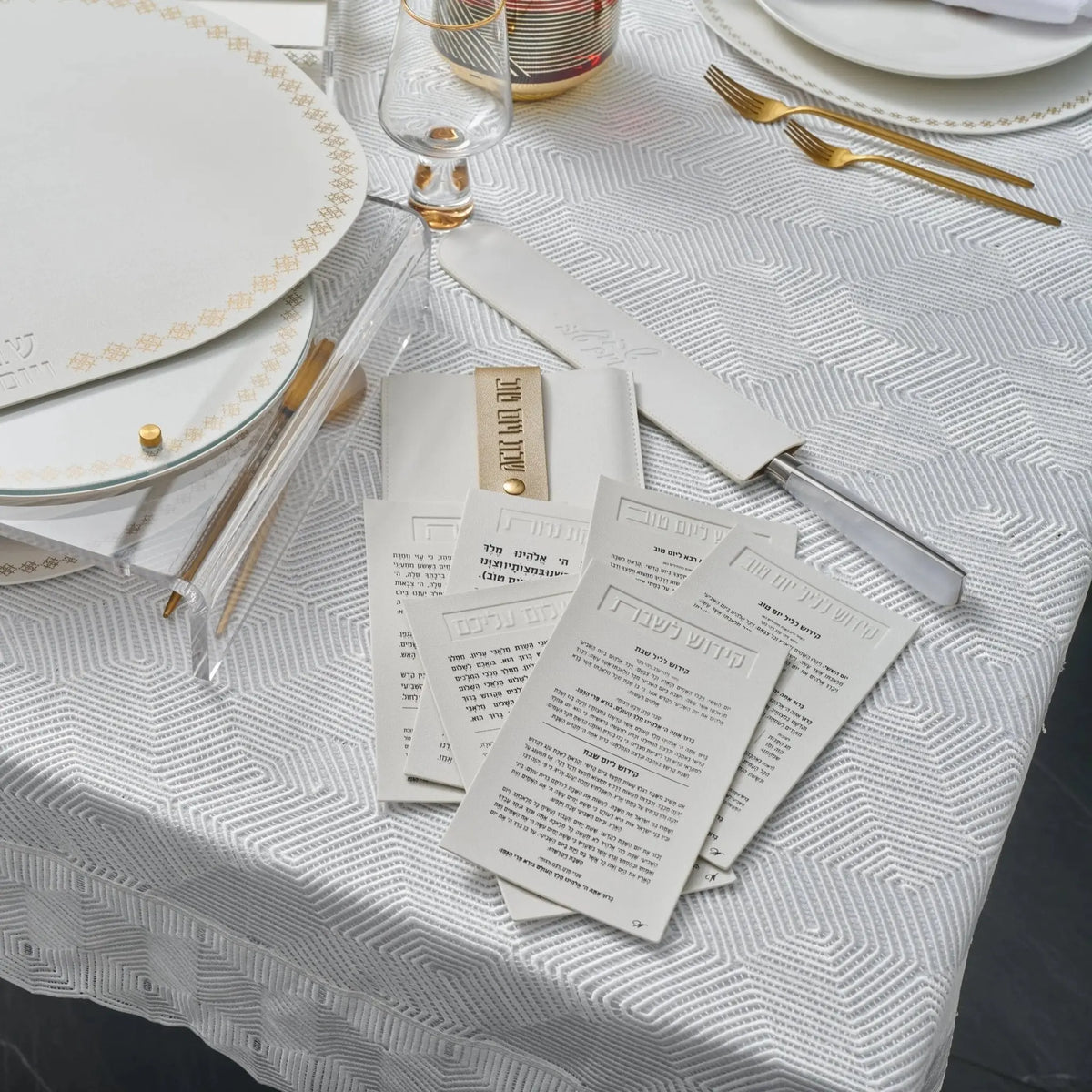 White leather Shabbos pouch displayed on white tablecloth with place setting, showing practical hostess gift for holiday entertaining.