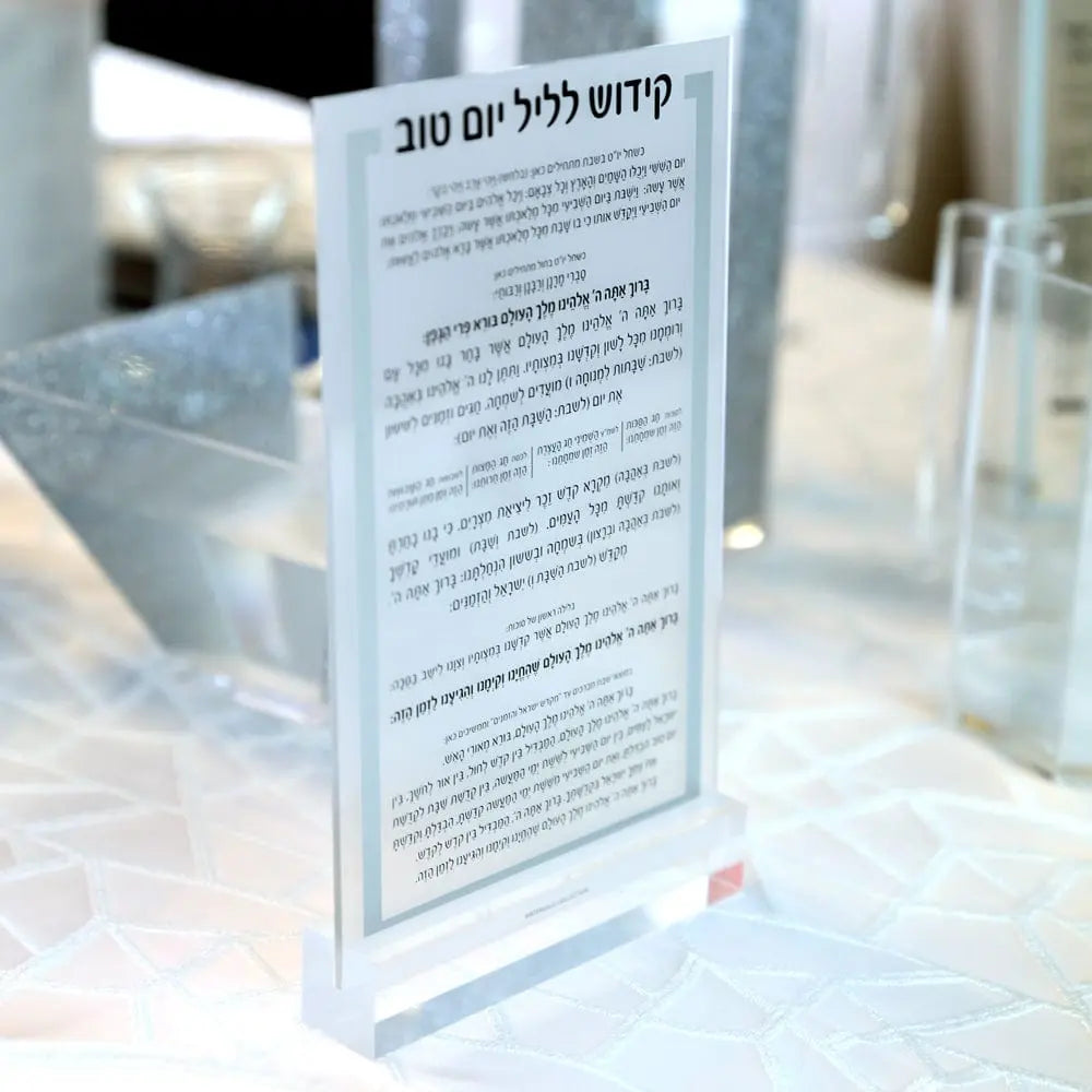 Silver-framed lucite Luxury Kiddush card by Waterdale Collection standing in a clear base on a white textured linen table, perfect for a contemporary Jewish holiday setting.