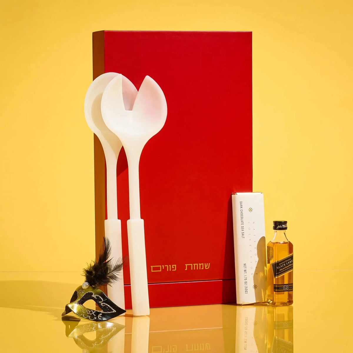 Cream and beige resin salad servers with heart-shaped handles displayed with red gift box and Purim accessories on yellow background.
