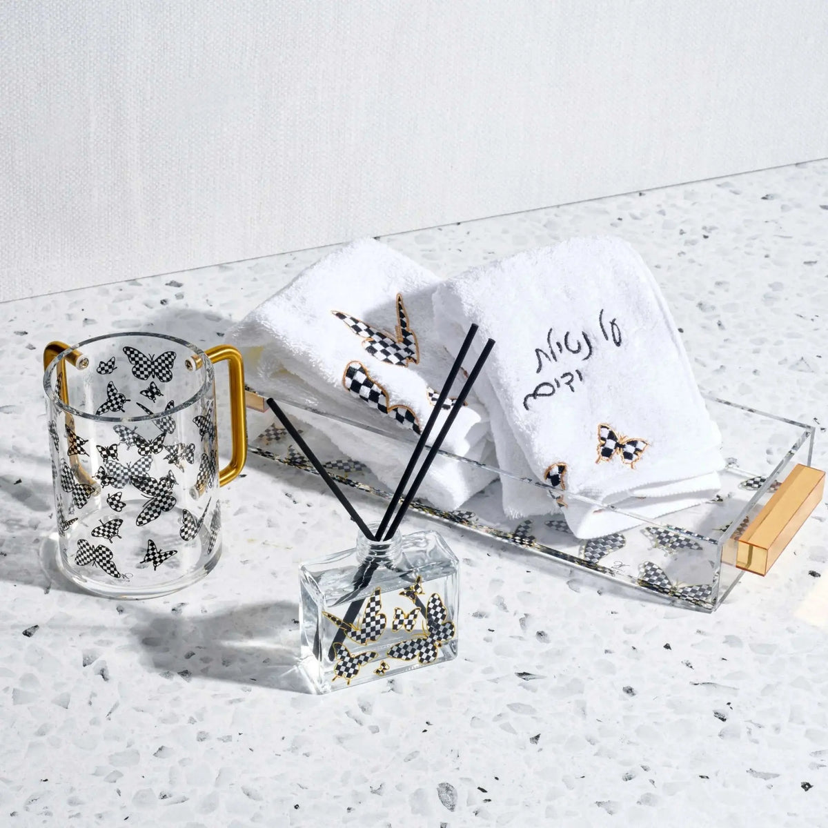 Netilas Yadayim Onyx Butterfly Hand Towel in gold and silver with matching toiletries displayed on marble surface