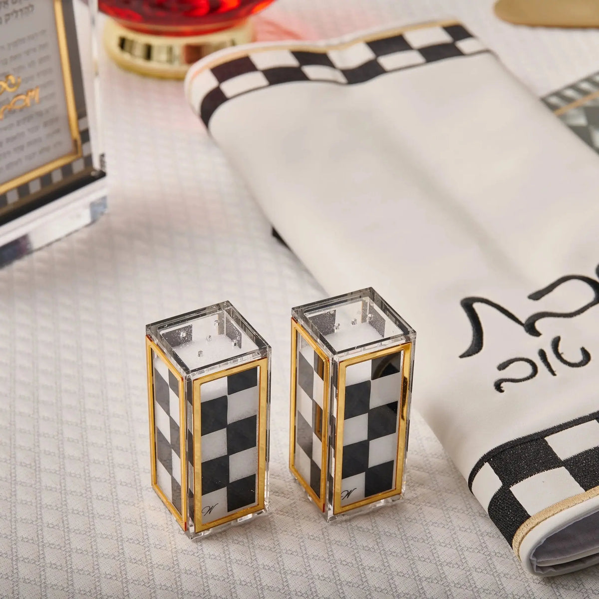 Pair of gold and black checkered onyx salt shakers displayed on white surface with tableware in background.