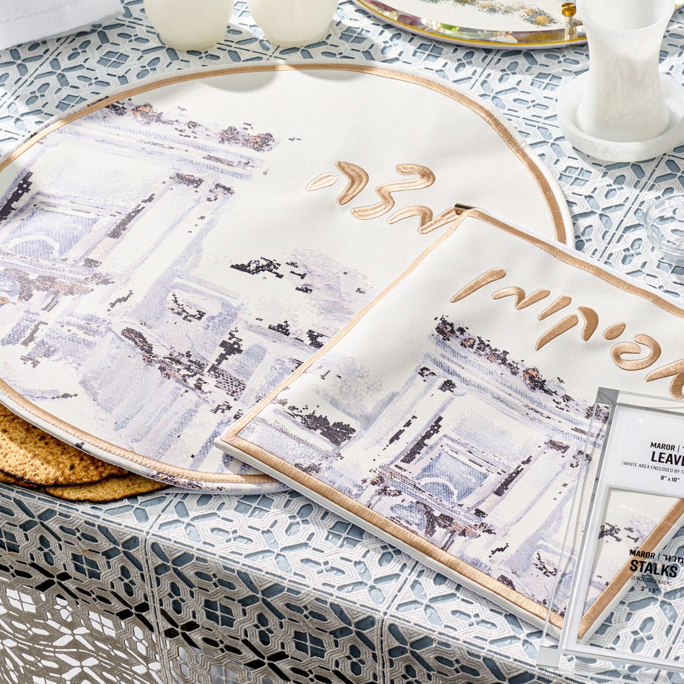 ainted Bais Hamikdash Pesach set including Seder plate and matzah cover with Jerusalem illustration and gold Hebrew lettering on a decorated table.