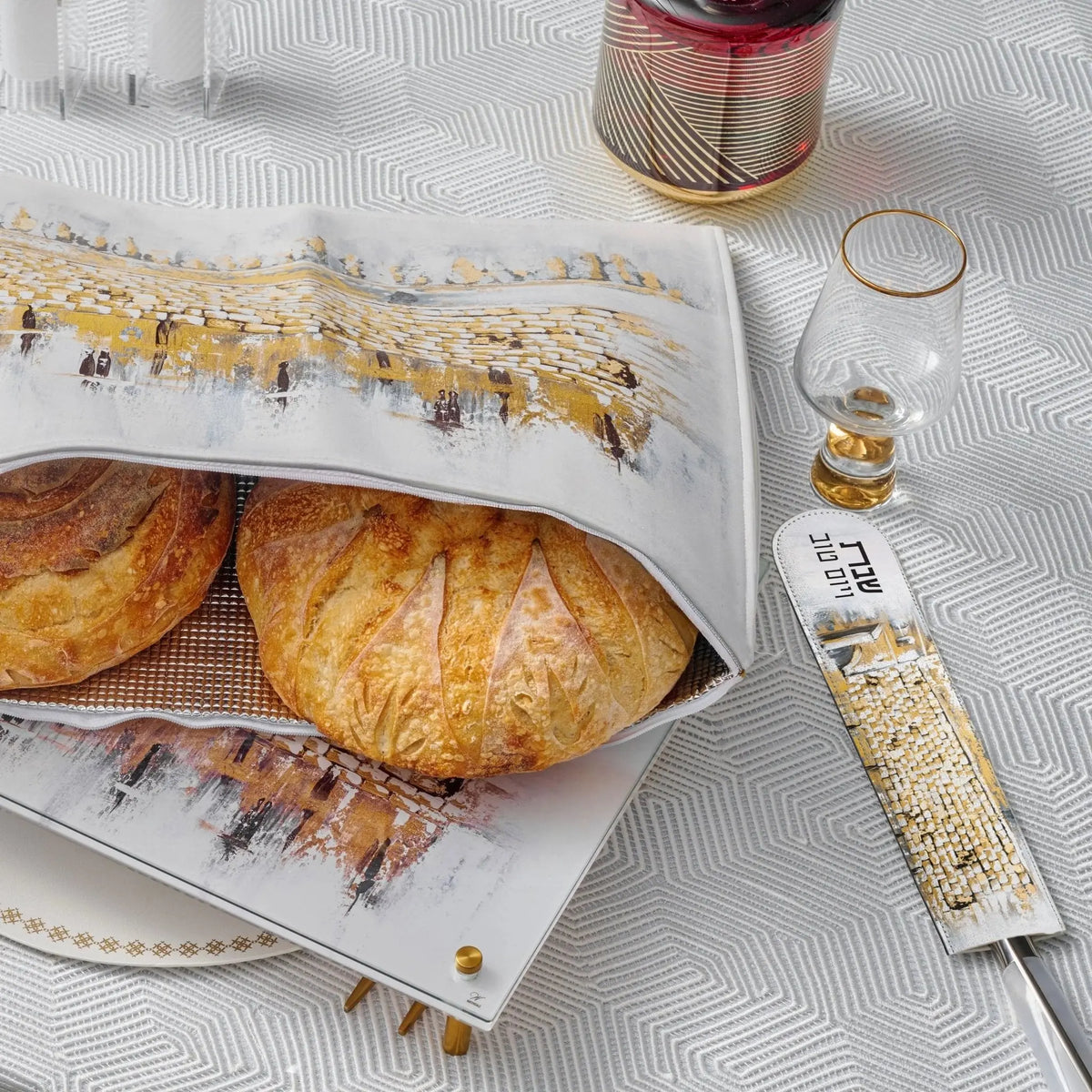 Painted Kosel knife blade cover in tan leather displayed next to challah bread and wooden board for Shabbat.