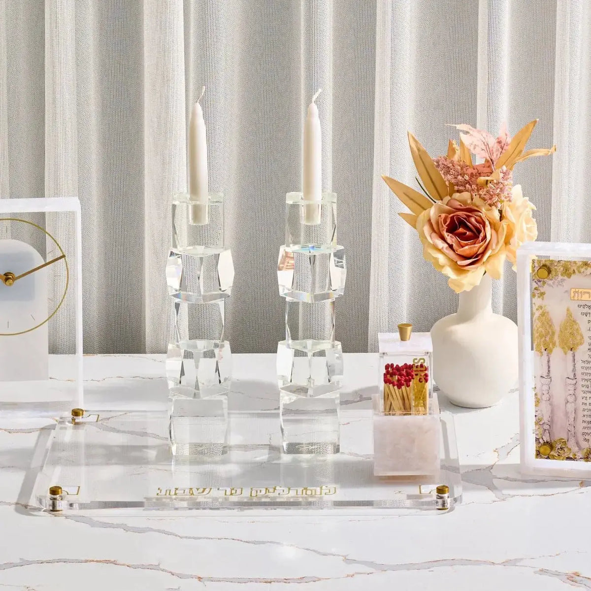 Pearlstone Hadlokas Neiros tray with glass candlestick holders on white marble surface, styled with white flowers and gold accents for Shabbat candle lighting.