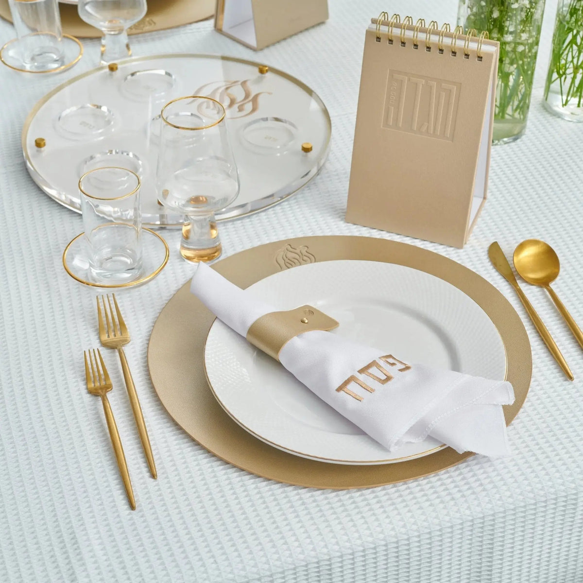 Pesach Leather Regal Round Chargers in cream with gold accents displayed on a holiday table setting with place settings and dinnerware.