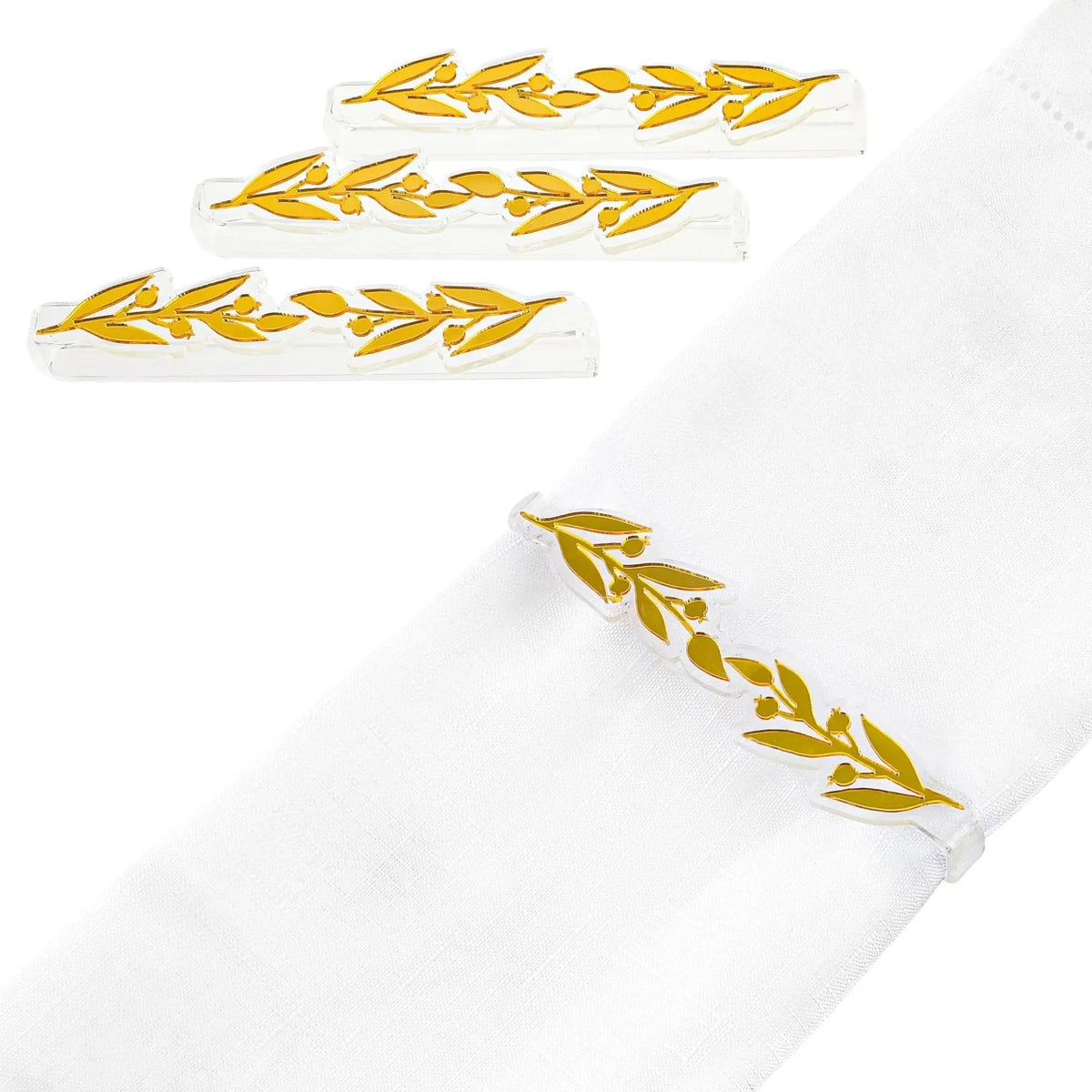 Gold pomegranate leaf napkin wraps arranged on white fabric, showing metallic leaf-shaped napkin rings from Waterdale Collection.