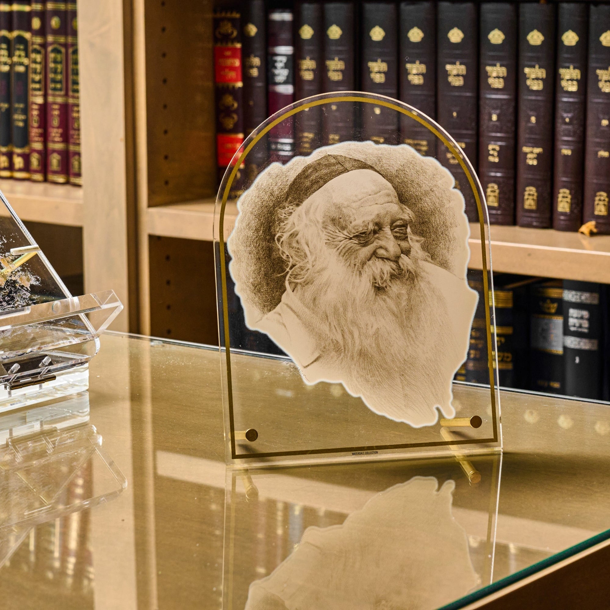 Rav Chaim Kanievsky Tabletop Gadol Sketch placed on a glass table in front of wooden bookshelves.
