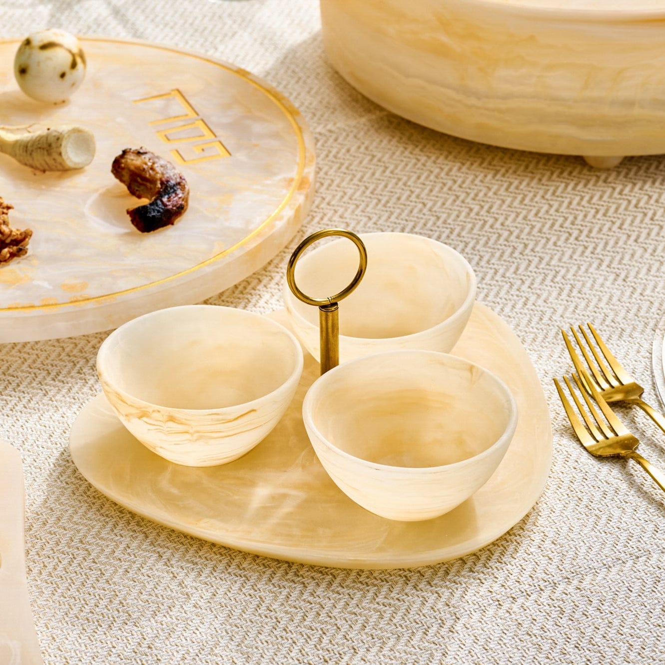 Resin Seder Plate Set featuring a marbled cream oval base with three coordinating bowls and a sleek gold-tone center ring handle, designed in warm neutral tones.