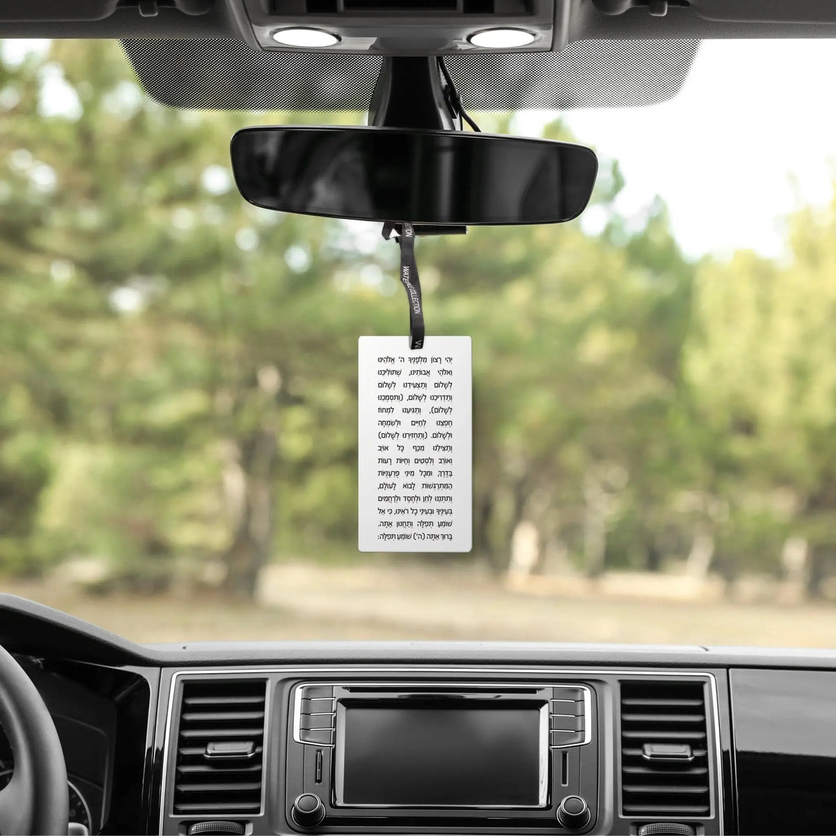 Scented Stone Tefillas Haderech Diffuser hanging from rearview mirror in car with forest background visible through windshield.