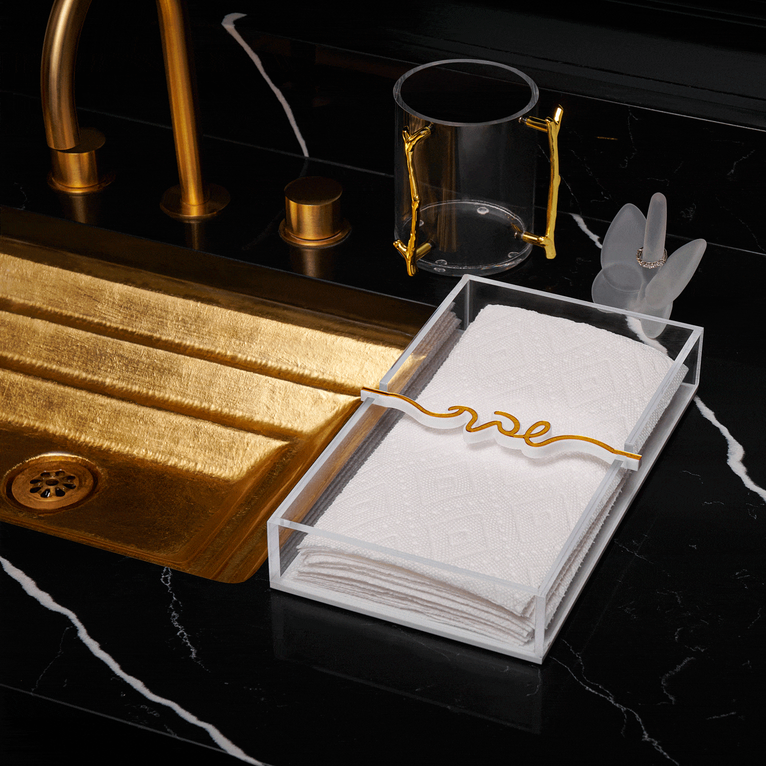 White Shabbos Bar paper towel holder with gold handles displayed on black marble countertop next to brass sink fixtures and accessories.