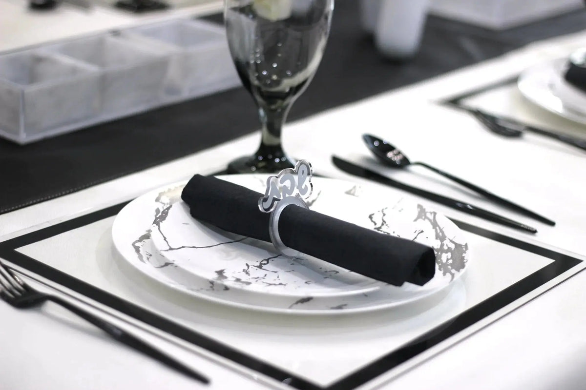 Elegant silver Shabbos napkin ring holding a black napkin on a formal place setting with white plate and silverware.