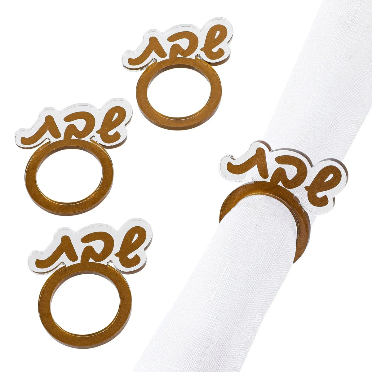 Four gold Shabbos napkin rings with Hebrew lettering displayed on white napkin, elegant tabletop décor for Shabbat meals.