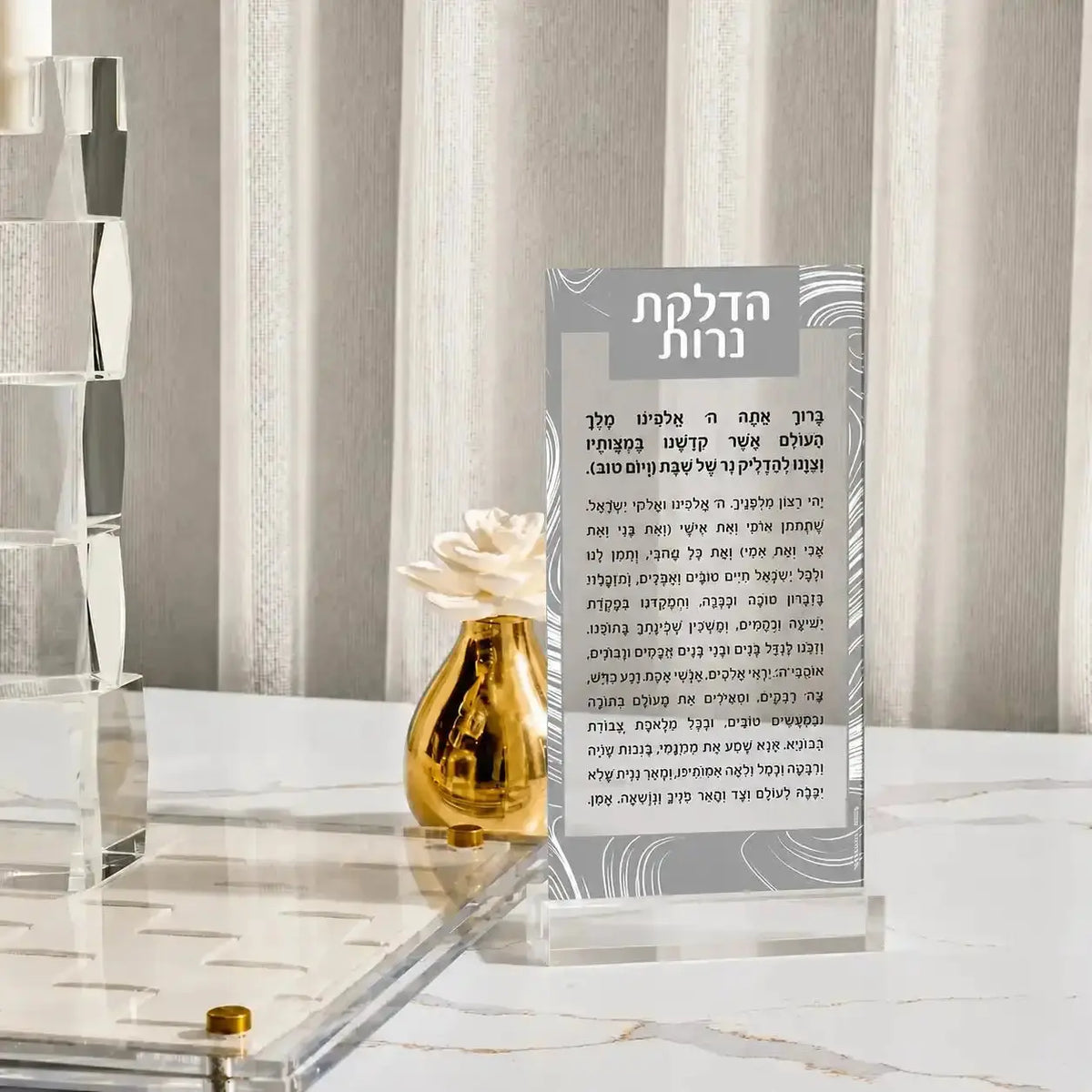 Gold swirl Hadlokas Neiros lucite card with silver text on white marble surface, Waterdale Collection Shabbat candle-lighting guide