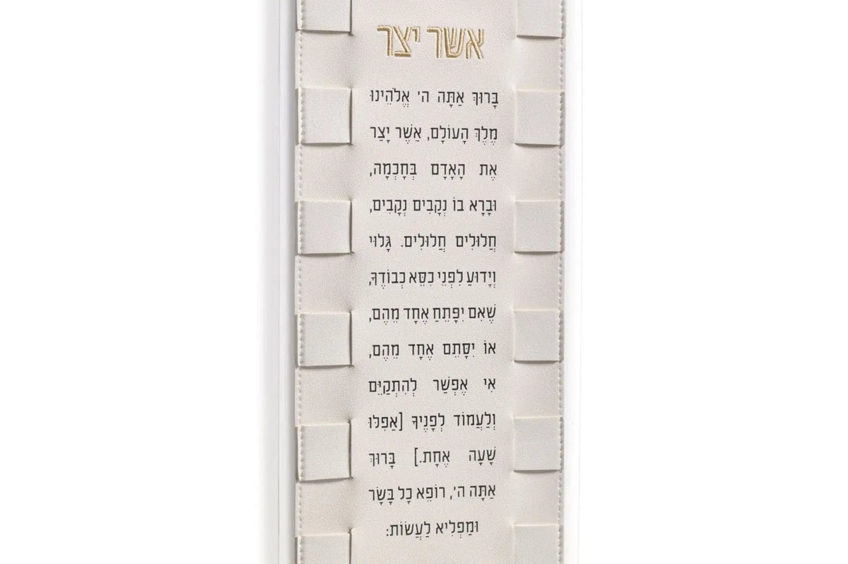 Woven Asher Yatzar wall art in cream with Hebrew text and textured brick-pattern background, mounted with metal corners.