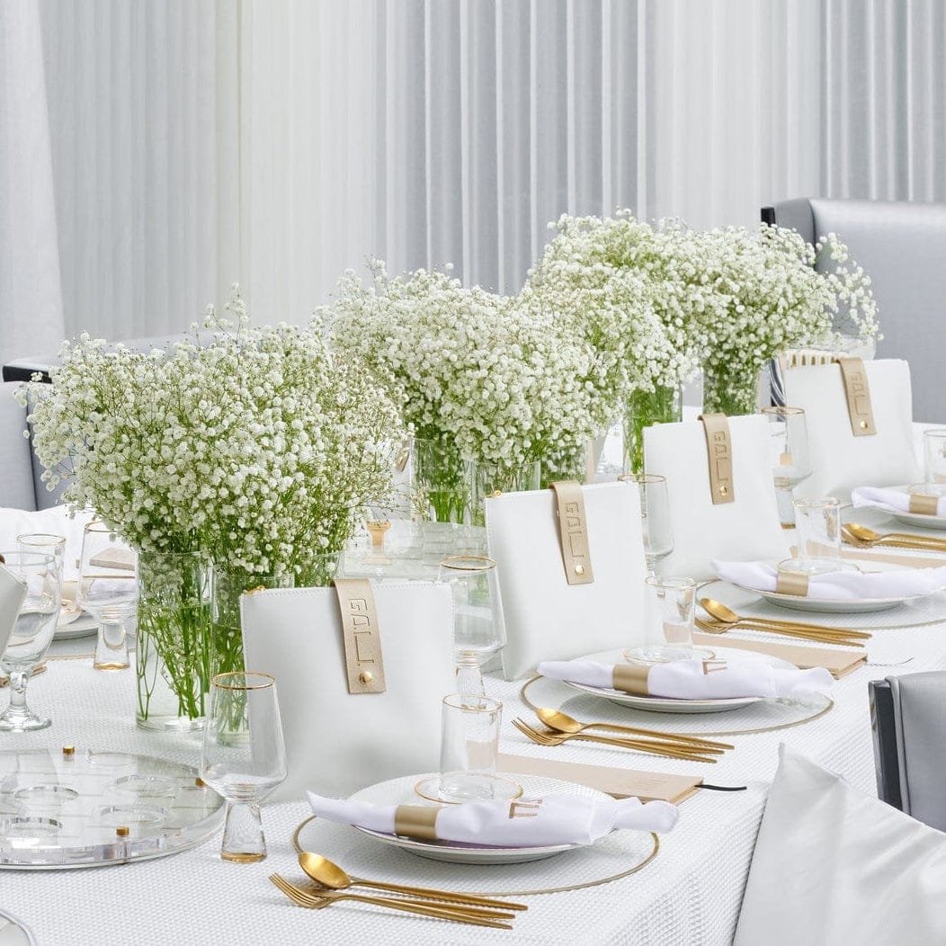 Elegant white and gold table setting with lush baby’s breath floral centerpieces in glass vases, gold flatware, white napkins, and modern place cards
