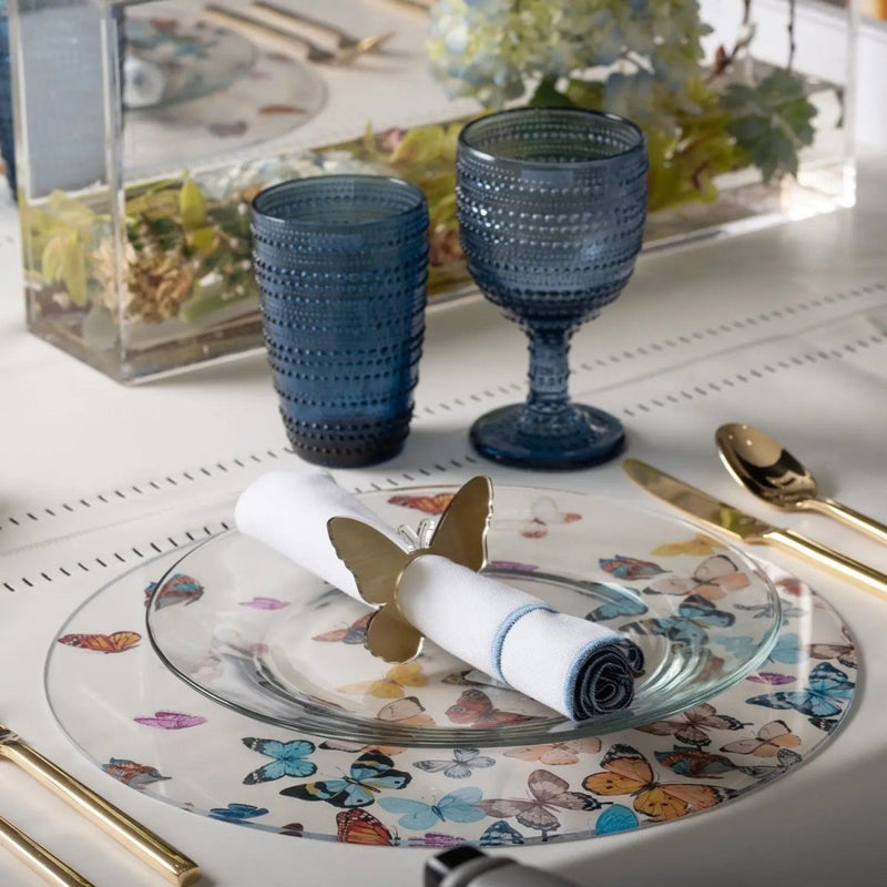 Butterfly Chargers in teal ceramic with gold butterfly accents, displayed on a white table with wine glasses and place settings.