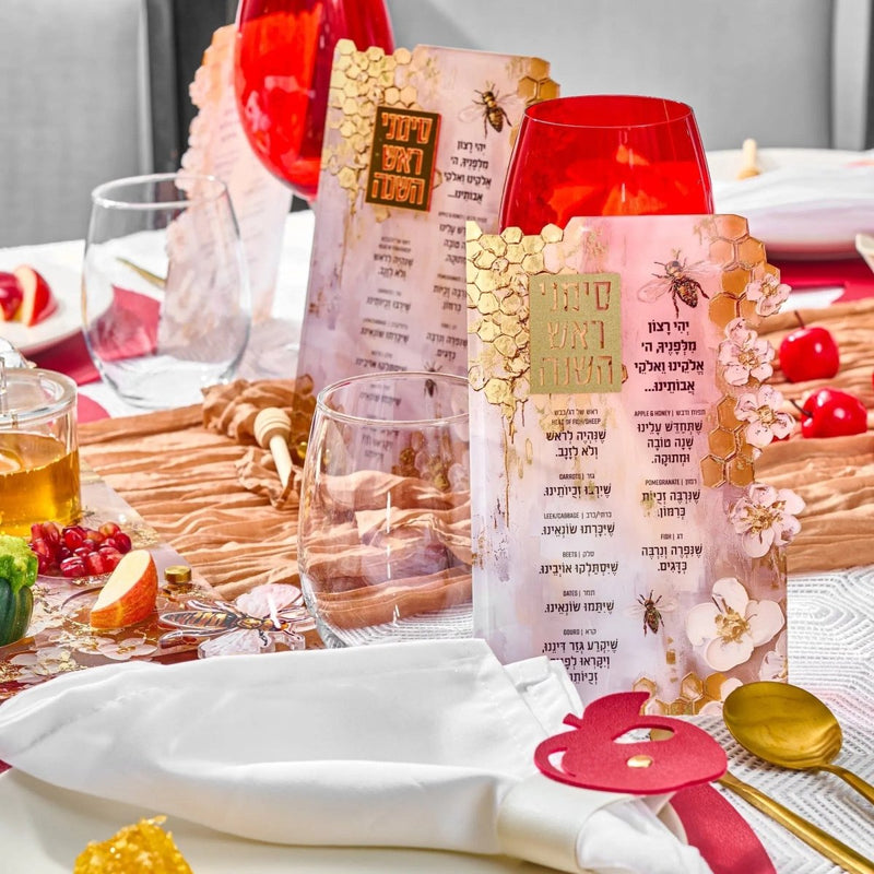 Honeycomb simanim card with painted design displayed among holiday decorations and ceremonial items on a white surface.