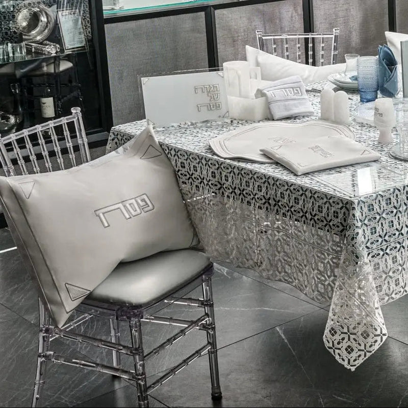 Pearlstone Pesach leather set displayed on patterned tablecloth with white pillows, plates, and place cards arranged on dining table with chrome chairs.