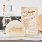 A small cream-colored  resin plaque with gold Hebrew lettering sits in front of a matching resin matchbo displayed on a white marble surface 