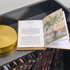 An open Hebrew leather tehillim book with printed text on one page and a tree illustration on the other, displayed on a dark shelf above other bound books.