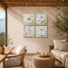 Four decorative viynl prints with Hebrew text and gold botanical illustrations arranged in a 2x2 grid on a beige wall in a sunlit succa