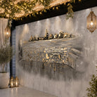 A large wall mural featuring a textured, abstract landscape with stone walls, trees, and water reflections, styled in a modern patio or hallway setting with hanging lanterns and plants.