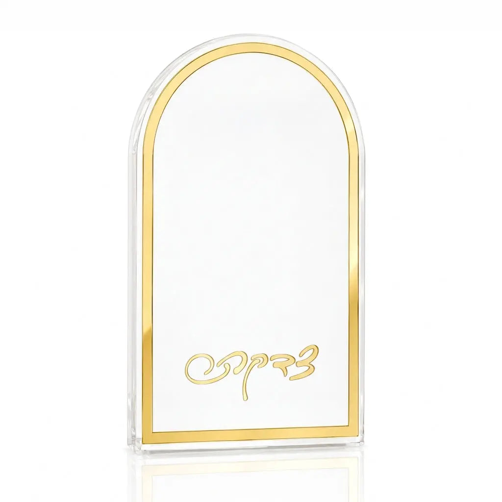 A clear Lucite arch-shaped tzedaka box with a polished gold border and gold cursive text at the bottom, displayed on a clean white background with a subtle reflection.