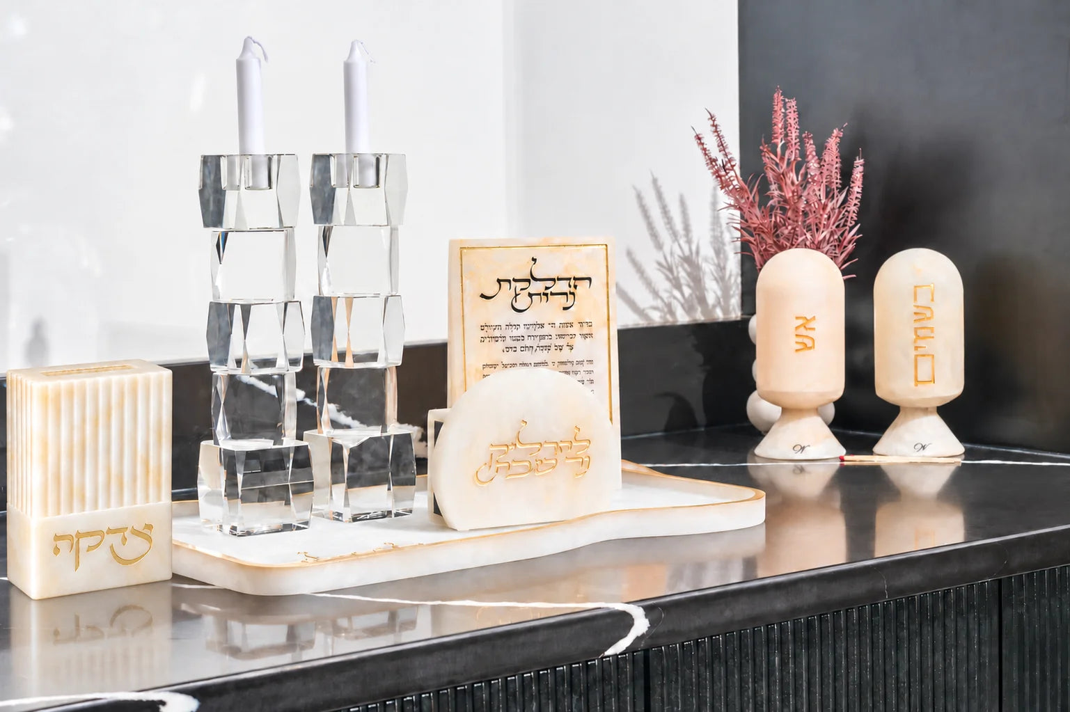 Gold resin Shabbat candle lighting set on a black counter with crystal candlesticks, a Hadlakas Neiros block, and match and spice cloches
