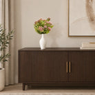 Tall white ceramic vase with pink faux flowers styled on a dark fluted sideboard beside a framed canvas